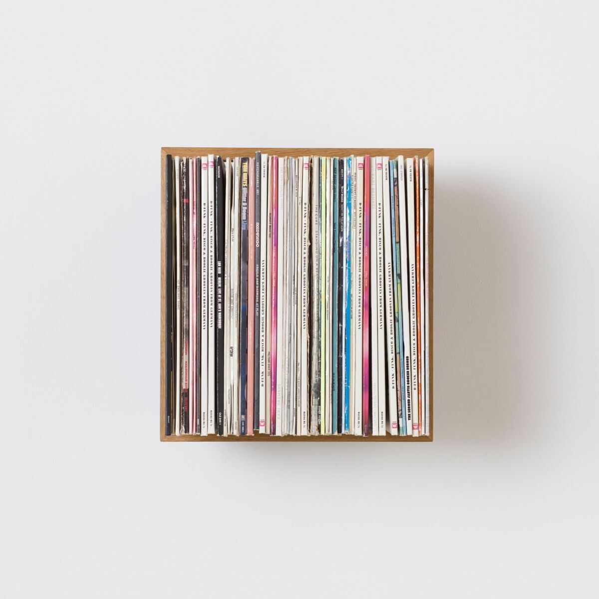 Ein Schallplattenständer aus Holz, gefüllt mit verschiedenen Vinyl-Platten, auf einem weißen Hintergrund.