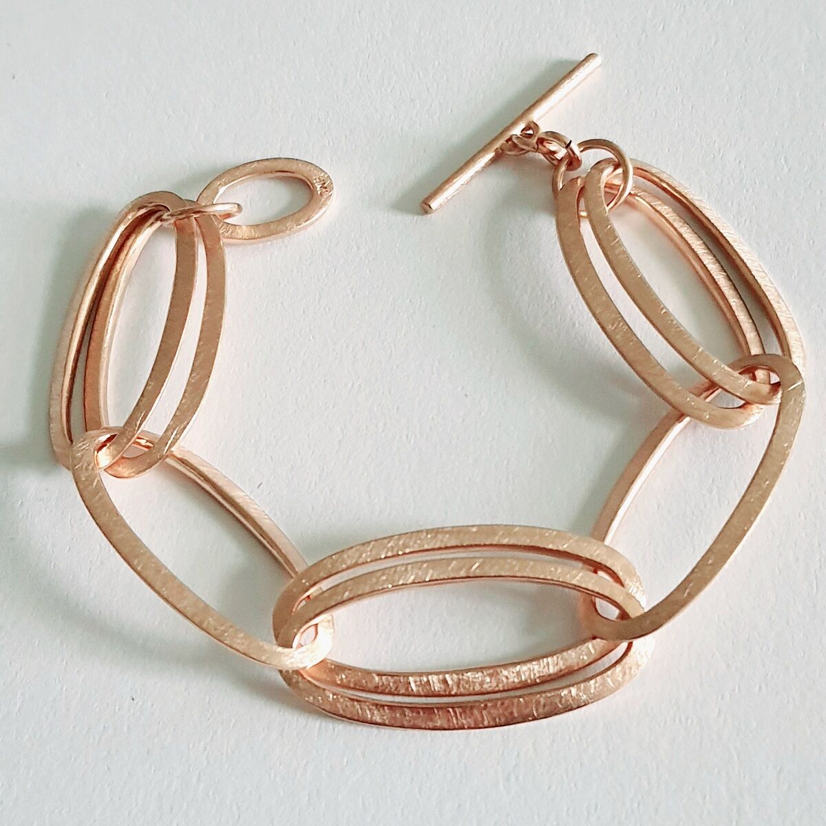 Ein elegantes Armband aus Roségold mit mehreren ovalen Gliedern und einem T-Verschluss. Das Design ist stilvoll und luxuriös.