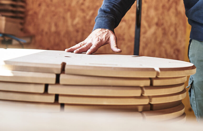Hand eines Handwerkers berührt gestapelte, zugeschnittene Holzplatten in einer Werkstatt