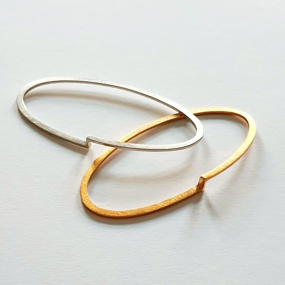 Zwei schlichte, elegante Armreife in Gold und Silber auf weißem Hintergrund.