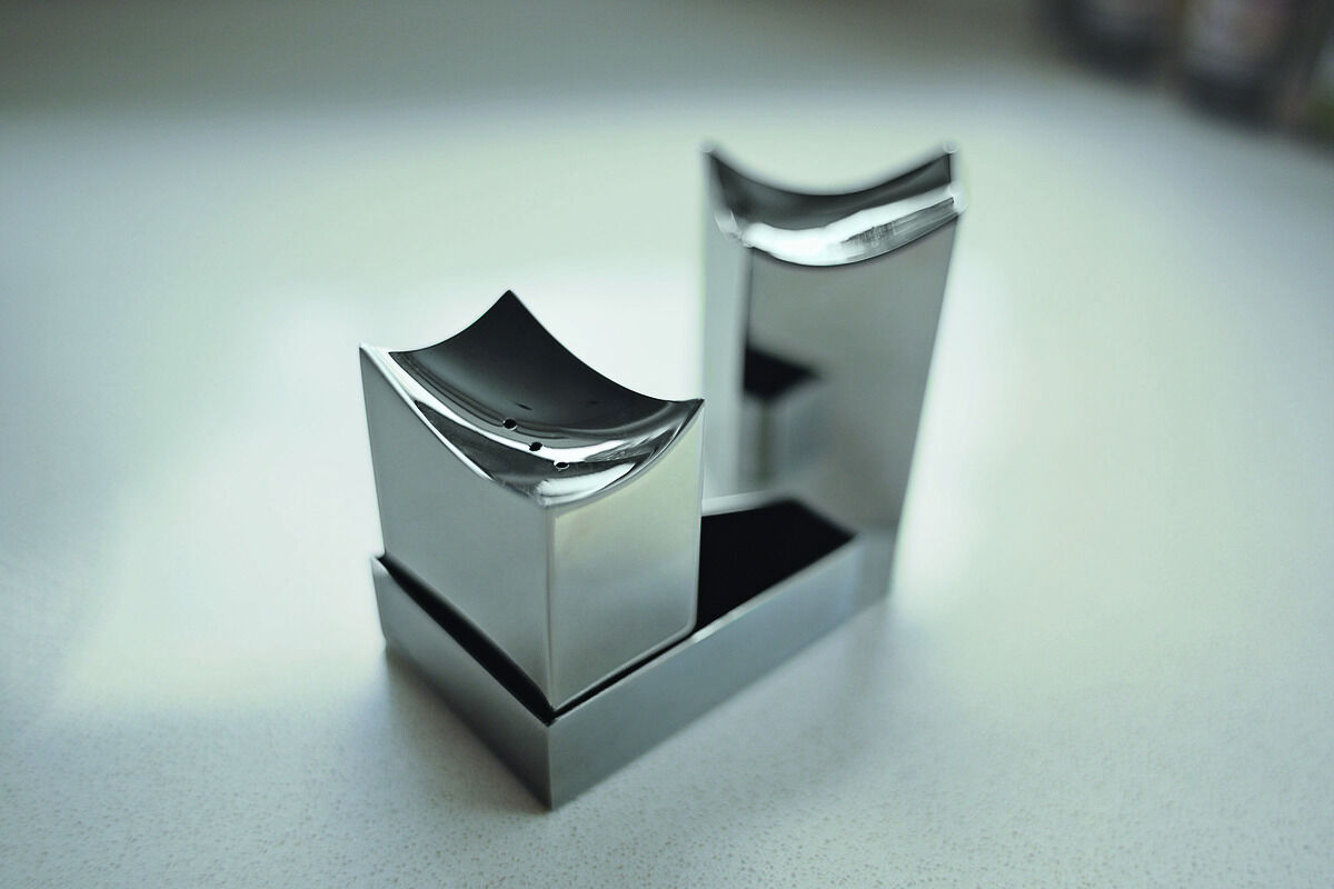 Ein Salz- und Pfefferstreuer-Set in Silber, das die Form der Elbphilharmonie nachbildet. Die beiden Streuer sind aus glänzendem Metall mit einem modernen Design und stehen auf einer schwarzen Basis.