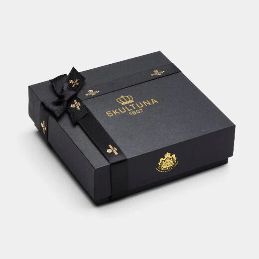 Quadratische, elegante Geschenkbox aus mattschwarzem Karton mit goldenen Schriftzügen und Emblemen der Marke SKULTUNA. Die Box ist mit einer schwarzen Schleife verziert und steht auf heller, neutraler Oberfläche. Hochwertige, luxuriöse Präsentationsverpackung für Schmuck.