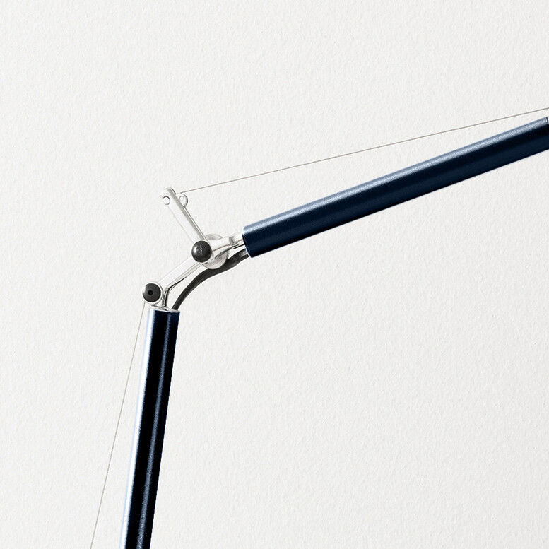 Detailaufnahme des oberen Arms einer Tischleuchte aus Aluminium in mattem Dunkelblau (RAL 5004), mit silbernen Verbindungsstücken und sichtbarer Seilzugmechanik vor einer weißen Wand. Das Design wirkt modern und technisch.