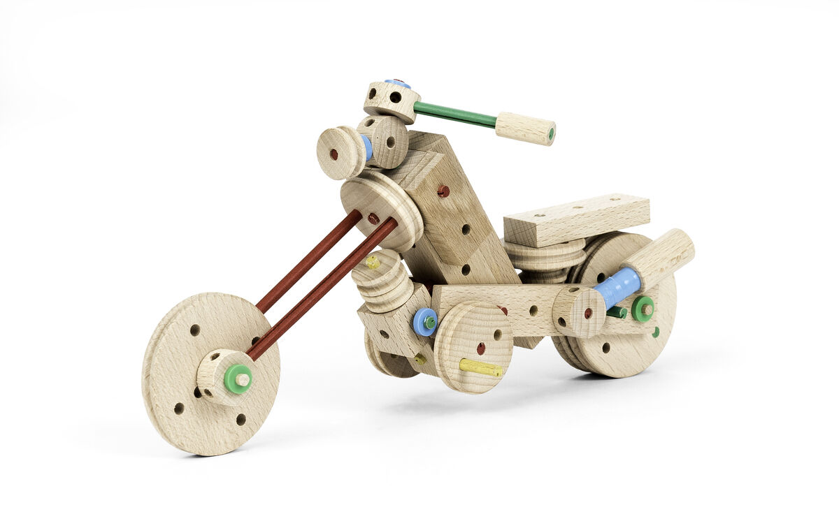 Das Bild zeigt ein aus Holz konstruiertes Modell eines Motorrads. Das Set, genannt 'Holzkonstrukionsbaukasten Explorer E318', besteht aus 318 Teilen und ist farblich mit Holztönen, Rot, Grün, Blau und Gelb gestaltet. Verschiedene Holzstücke und Rundstäbe sind ineinander gesteckt und geschraubt, um die Form eines Motorrads zu bilden.