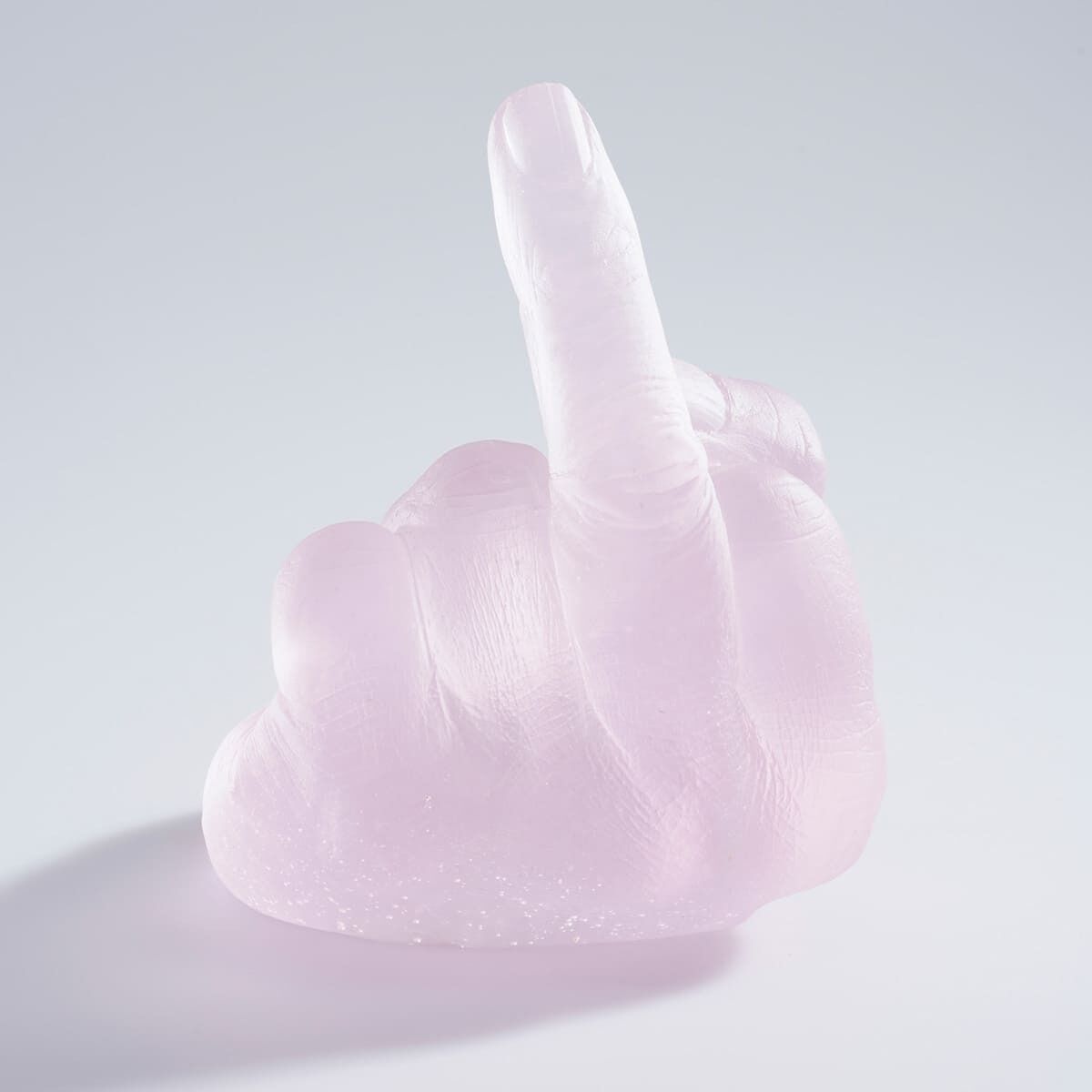 Eine Glas-Skulptur von Ai Weiwei, die eine Hand darstellt, die den Mittelfinger zeigt. Die Skulptur ist in einem hellrosa Farbton gehalten und beeindruckt mit einer detaillierten und realistischen Darstellung.