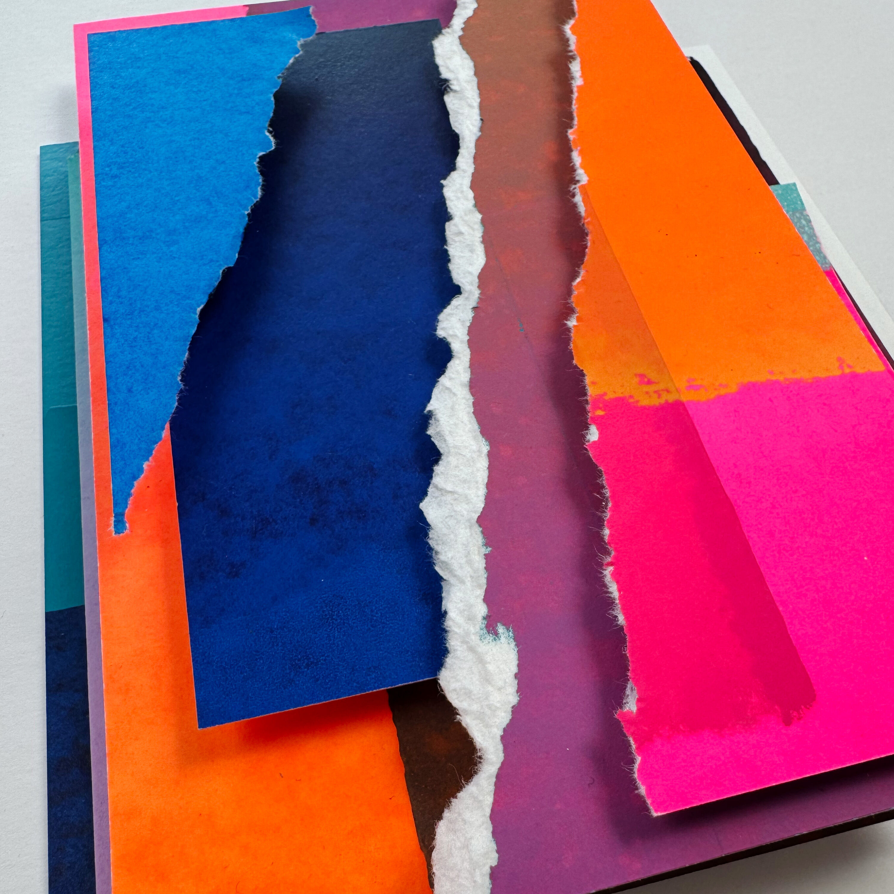 Das Bild zeigt eine abstrakte Collage aus mehreren übereinandergelegten Papierflächen mit unterschiedlichen Farben wie Blau, Pink, Orange, Türkis, Weiß und Schwarz. Die Komposition wirkt modern und lebendig durch die kräftigen Farbtöne und unterschiedlichen Texturen. Geeignet als dekoratives Unikat für zeitgenössische Wohneinrichtungen oder als Geschenk für Kunstinteressierte.