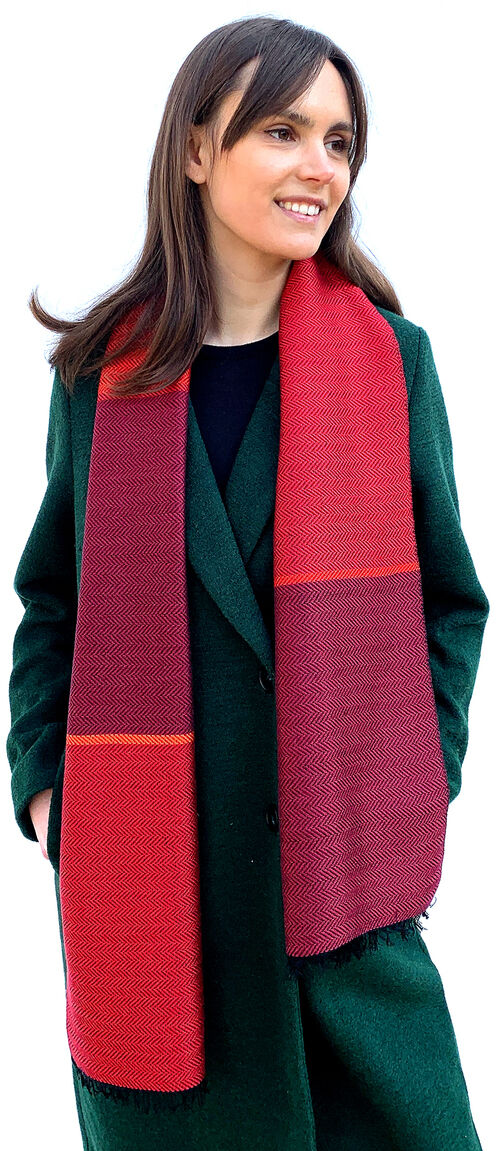 Frau trägt einen roten Seidenschal mit Fischgratmuster und einen grünen Mantel. Sie lächelt und schaut zur Seite. Der Schal ist elegant und stylisch, ideal für kältere Jahreszeiten.