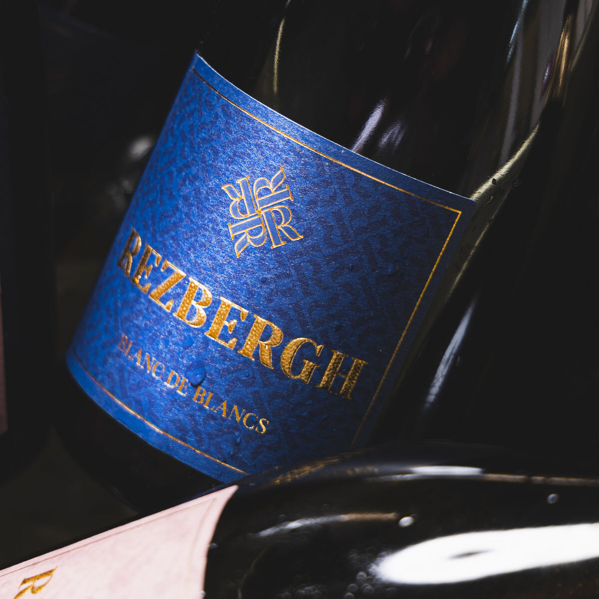 Eine edle Flasche Crémant de Luxembourg BLANC DES BLANCS brut mit einem blauen und goldenen Etikett steht im Vordergrund. Die Flasche wirkt luxuriös und ist ideal für festliche Anlässe oder als Geschenk geeignet.