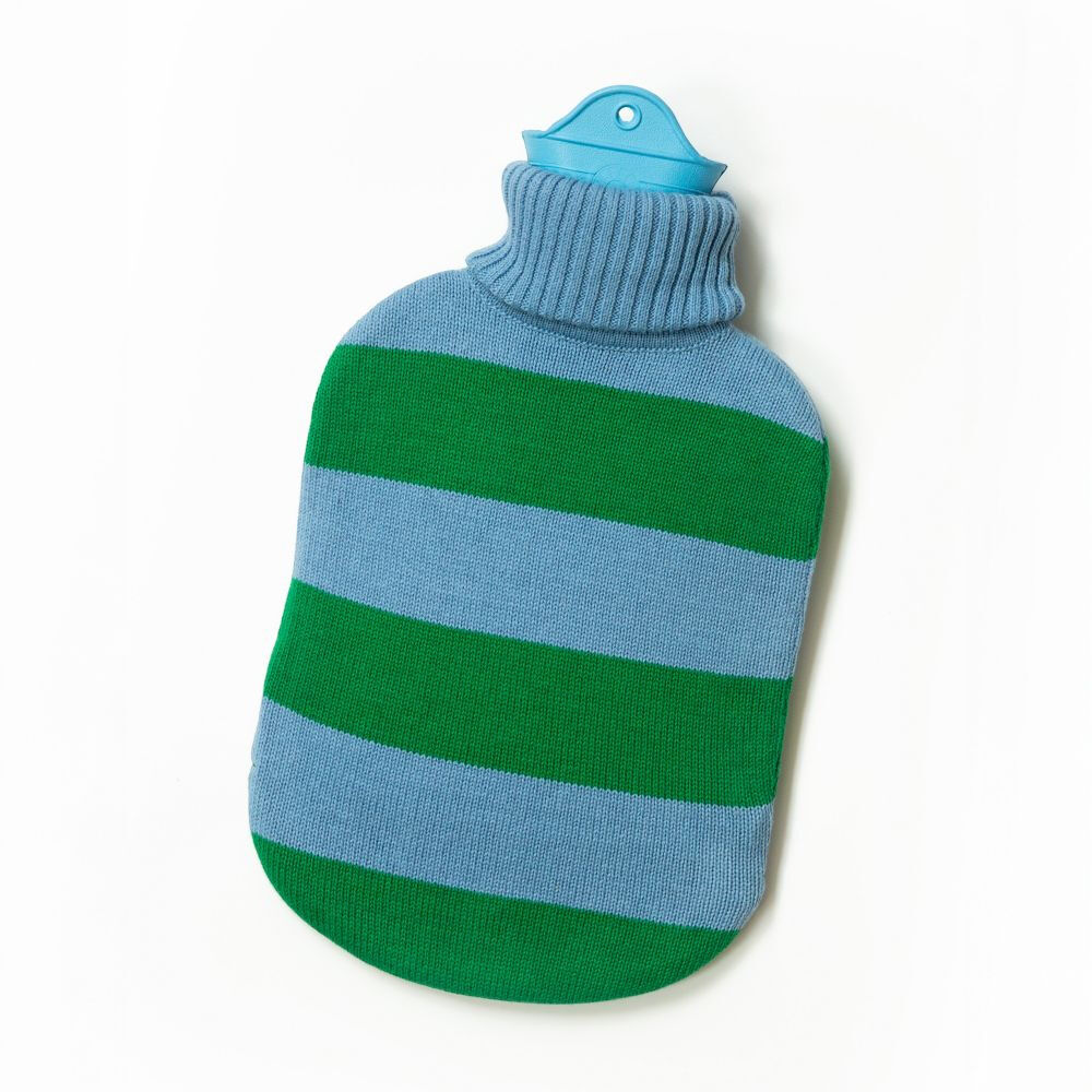 Schräg liegende SUITE702 Wärmflasche »gestreift« vor weißem Hintergrund. Der weiche, fein gestrickte Bezug zeigt breite horizontale Streifen in Himmelblau und Grün, einen gerippten hellblauen Rollkragen sowie einen abgerundeten Boden. Oben ragt der türkisfarbene Latexverschluss mit Aufhängeloch heraus.