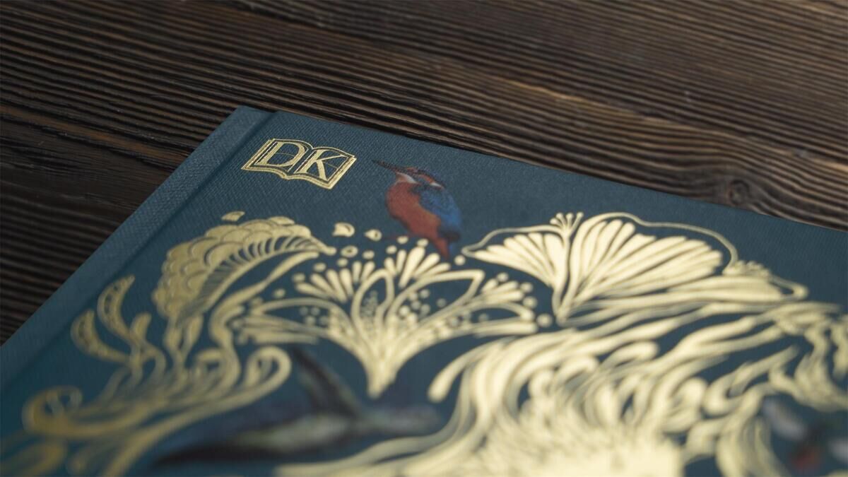 Ein Nahaufnahme des Buchcovers von 'Wundervolle Welt der Tiere' zeigt detaillierte goldene Illustrationen von Pflanzen und einen kleinen Vogel auf einem blauen Hintergrund.