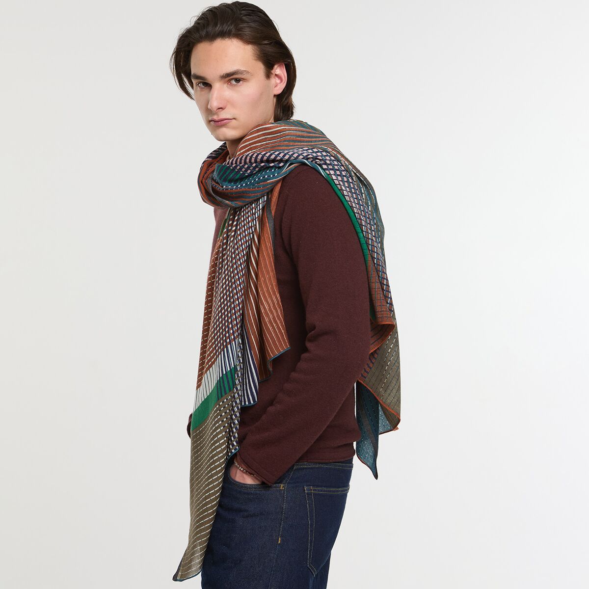 Person trägt einen großen Wollschal mit Streifenmuster in verschiedenen Braun- und Naturtönen, kombiniert mit einem braunen Pullover und dunkler Jeans. Der Schal wirkt warm und gemütlich, ideal für Herbst und Winter.