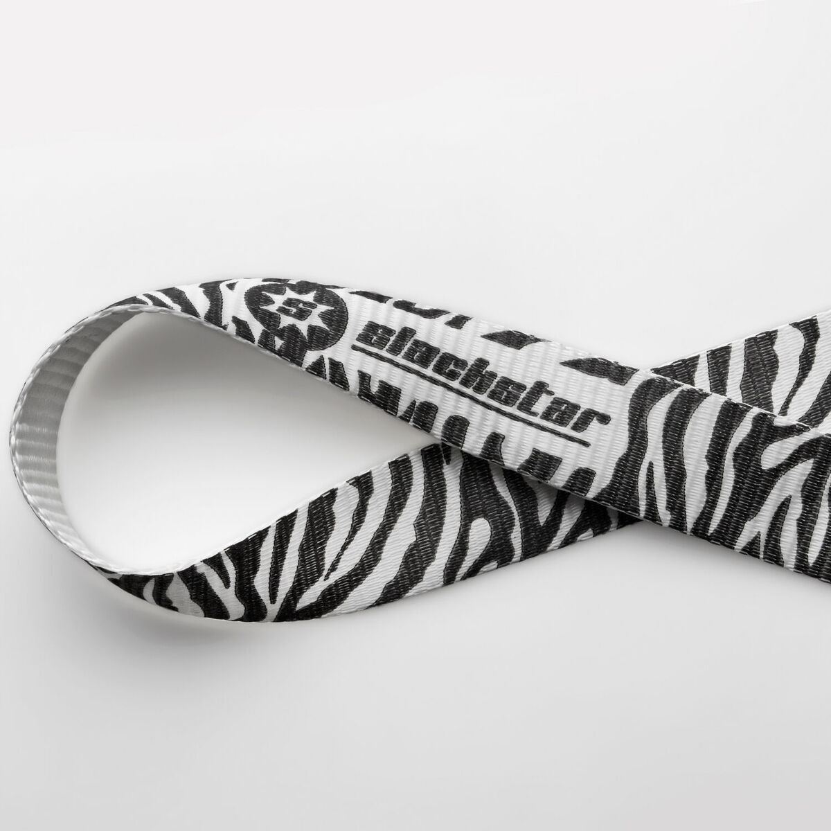 Ein Bild einer Slackline mit Zebra-Muster. Es hat schwarze und weiße Streifen und das Logo des Herstellers ist darauf gedruckt. Das Band ist zu einer Schleife geformt.
