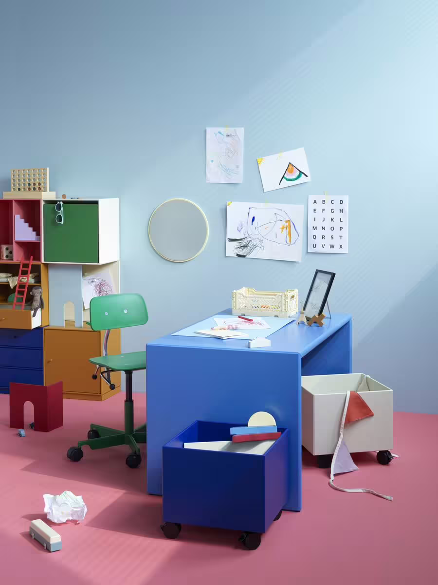 alt="Buntes Kinderzimmer mit verschiedenen Ordnungssystemen an und um einen kleinen Schreibtisch herum"
