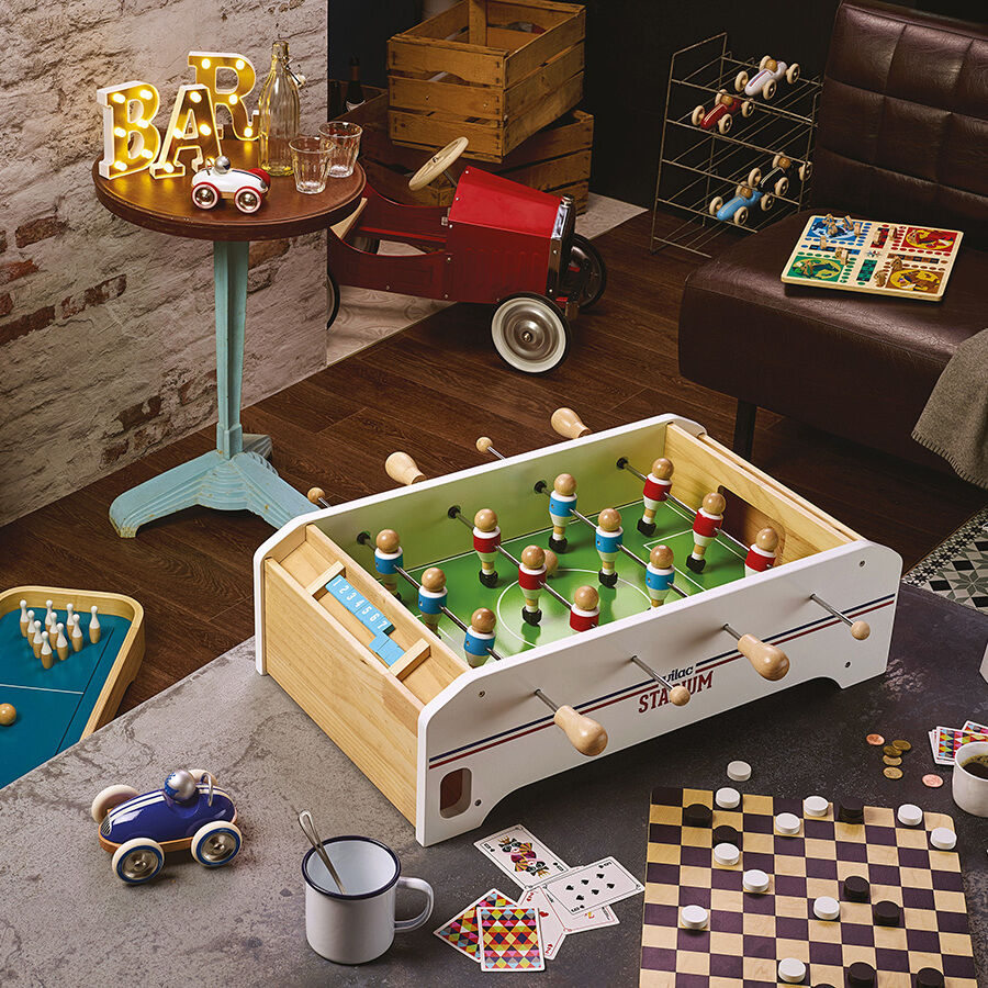 Ein gemütliches Spielzimmer mit einem Tischfußballspiel, umgeben von verschiedenen Spielzeugen und Dekorelementen. Der Raum ist warm und einladend eingerichtet mit Holzböden und einer rustikalen Ziegelwand.