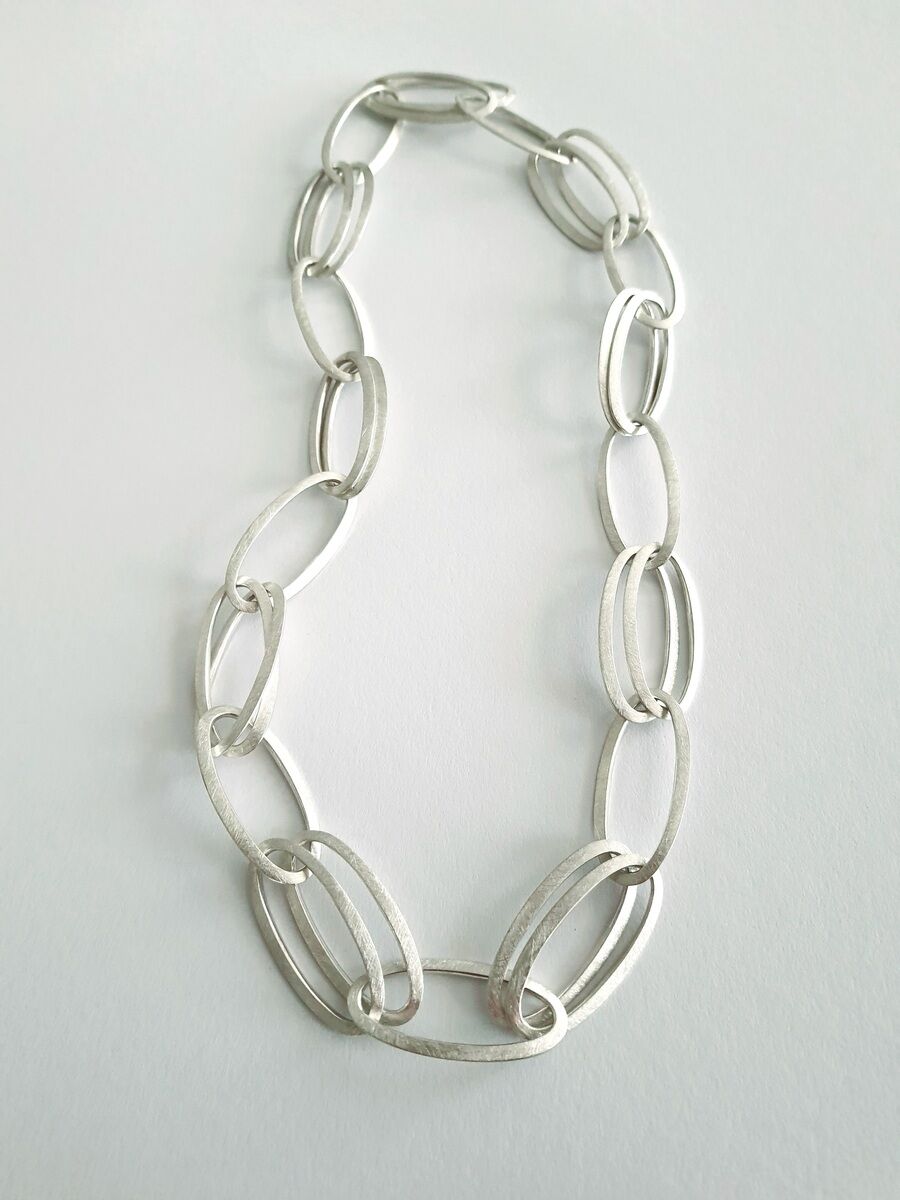 Silberne Halskette mit großen, ovalen Gliedern auf weißem Hintergrund. Die schlichte und elegante Kette hat ein minimalistisches Design und besteht aus miteinander verbundenen, glänzenden Ovalen.