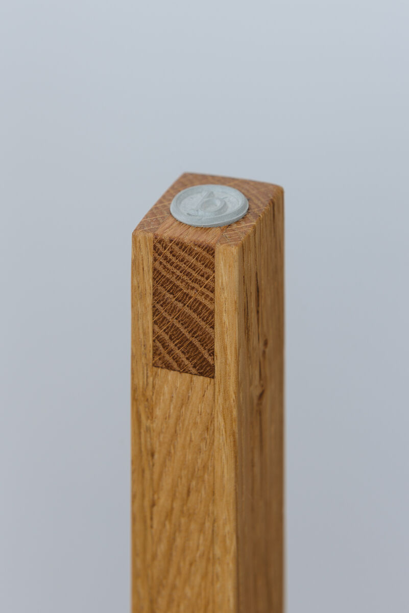 Nahaufnahme eines Stehpults aus Holz mit einer metallischen Münze oben aufgesetzt. Das Design ist minimalistisch und die Oberfläche aus natürlichem Holz wirkt elegant.