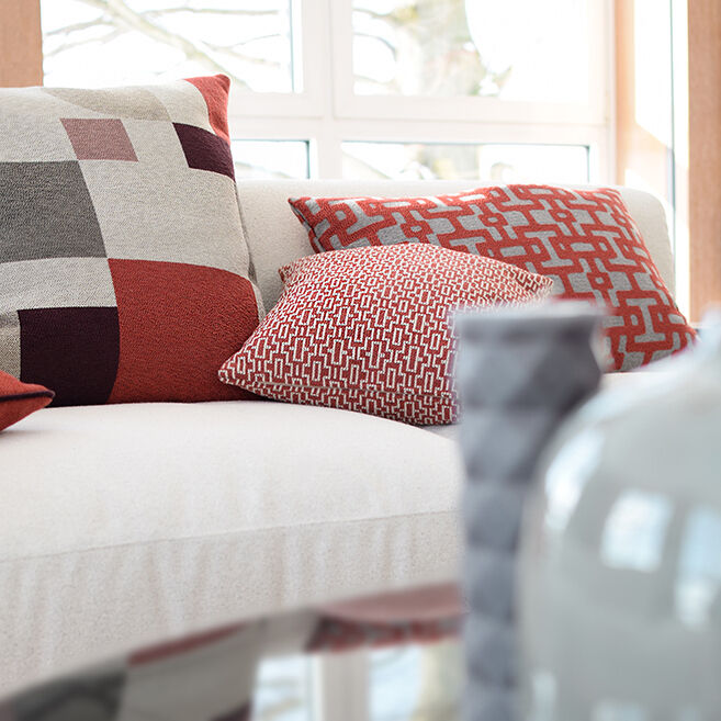Kissen auf einem Sofa mit modernem grafischem Muster in Rot, Grau und Weiß, platziert in einem freundlich beleuchteten Raum.