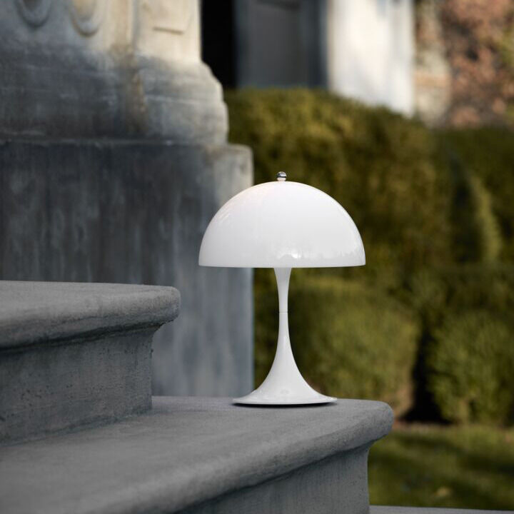 Tischleuchte Panthella 250 in Acryl Opal Weiß auf einer steinernen Treppe, moderner und eleganter Stil, Hintergrund mit bewachsenen Wänden und Büschen.