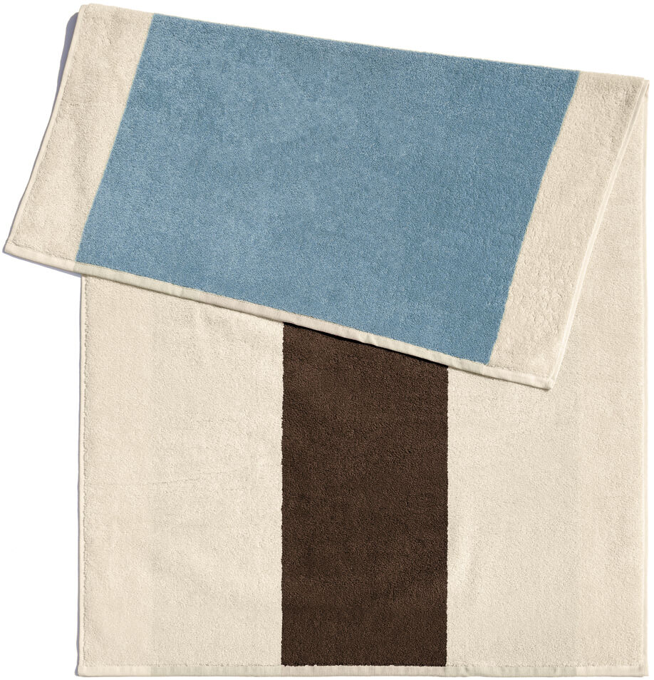 Ein Badematte in den Maßen 50 x 80 cm mit einem schlichten Design. Die Matte hat eine dominante weiße Farbe mit einem breiten braunen Streifen in der Mitte und einem blauen Abschnitt auf einer Seite. Perfekt für moderne Badezimmer zur Nutzung nach dem Duschen oder Baden.
