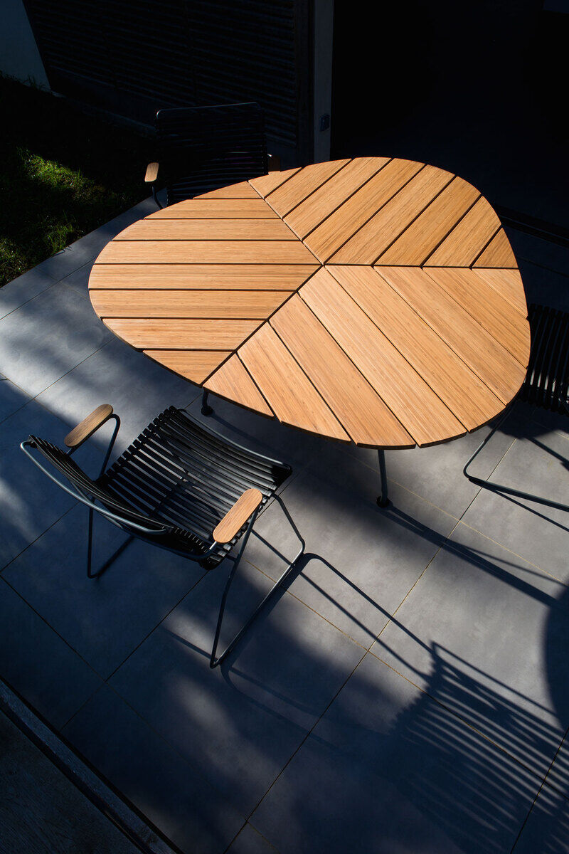 Moderner Gartentisch namens 'LEAF' mit einzigartigem Holzdesign, umgeben von stilvollen schwarzen Gartenstühlen, auf einer hellgrauen Terrasse.