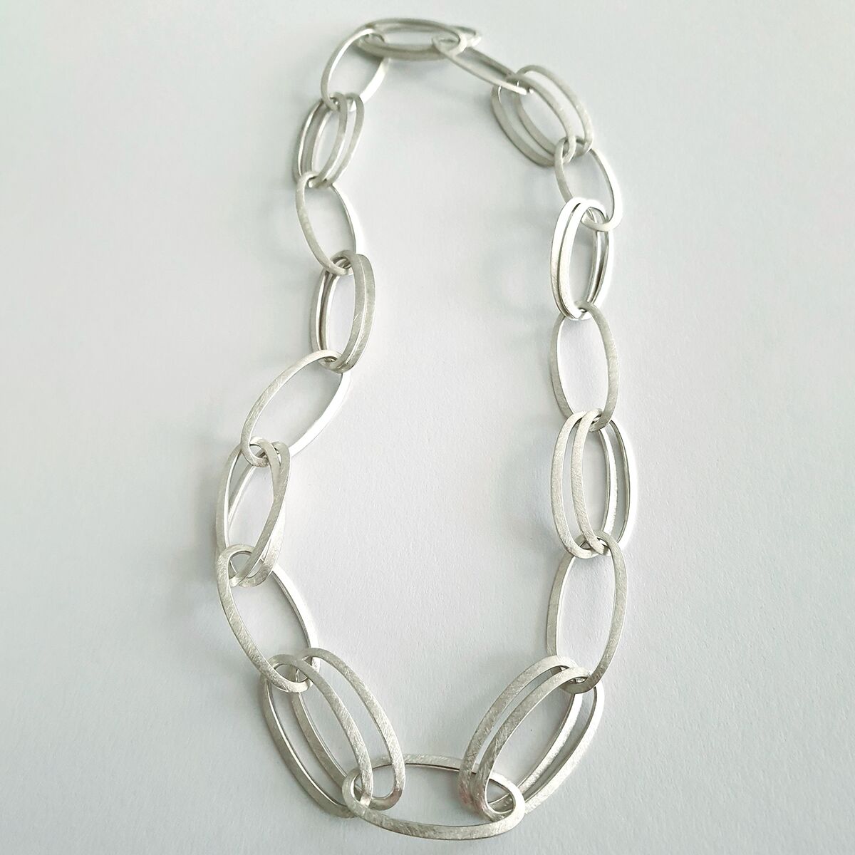 Abgebildet ist das HML-Collier »GRACE« aus 925er Silber von HML Berlin. Die Kette besteht aus großen, ovalen Gliedern mit matter Oberfläche und liegt auf weißem Untergrund. Das Design wirkt modern, puristisch und handgefertigt.