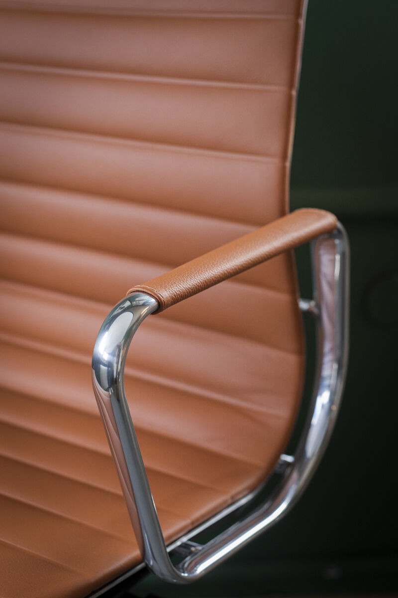 Nahaufnahme eines Vitra Alu Chair EA 118 mit poliertem Rahmen und brauner Lederpolsterung