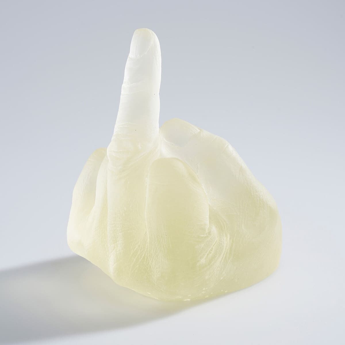 Eine transparente Glasskulptur von Ai Weiwei, welche eine Hand darstellt, die den Mittelfinger zeigt. Das Kunstwerk steht vor einem neutralen Hintergrund.