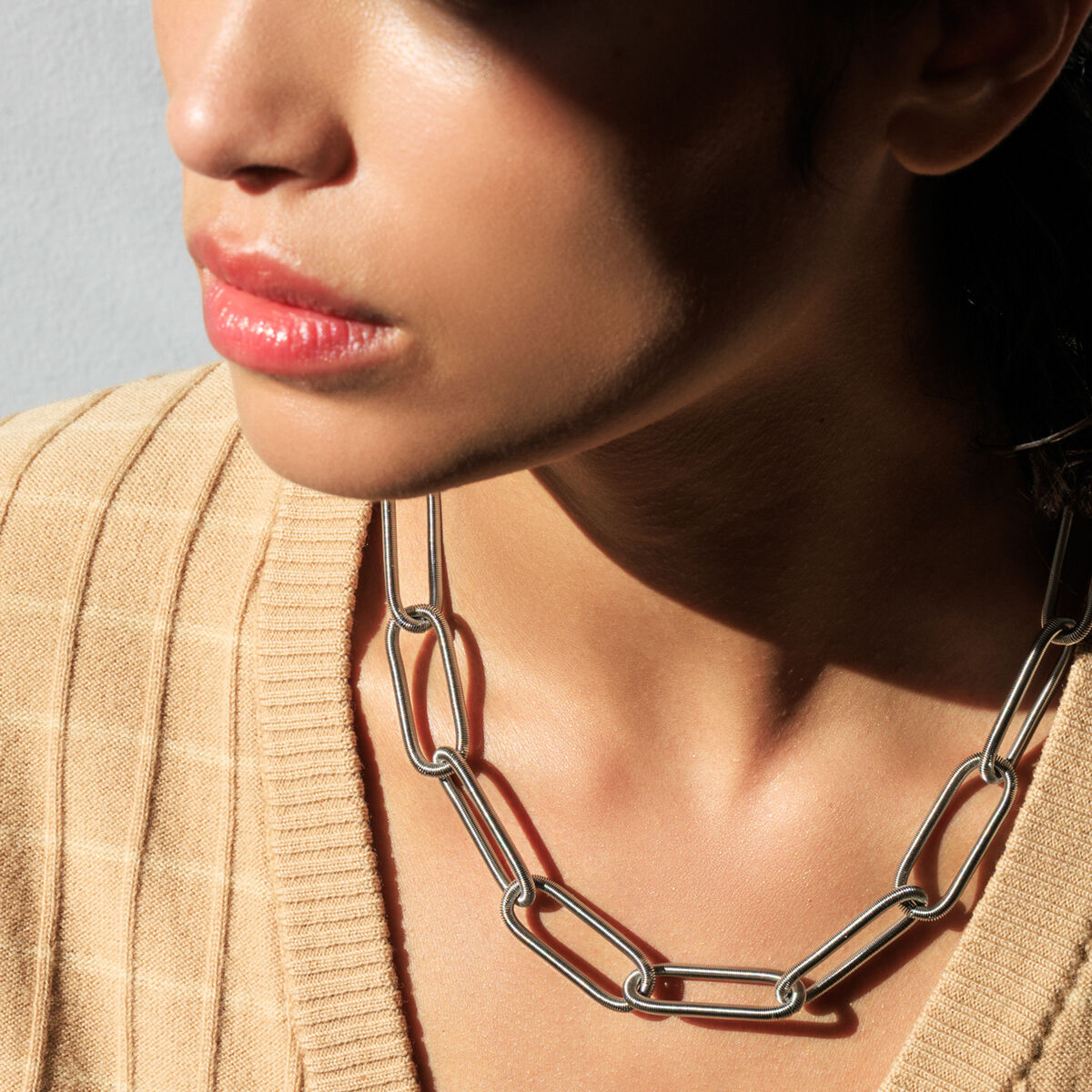 Eine Frau trägt das Collier "CHAIN" der Marke la molla aus Edelstahl. Die Kette ist mittellang, besteht aus großen, rechteckigen Gliedern und wirkt modern sowie auffällig. Das Licht erzeugt einen sanften Schatten auf Haut und beigem Oberteil.