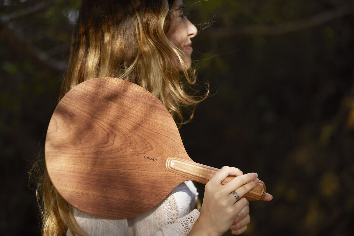 Eine Frau hält ein Beachball-Set aus Holz in der Hand. Im Hintergrund sind Bäume und Grün zu sehen.