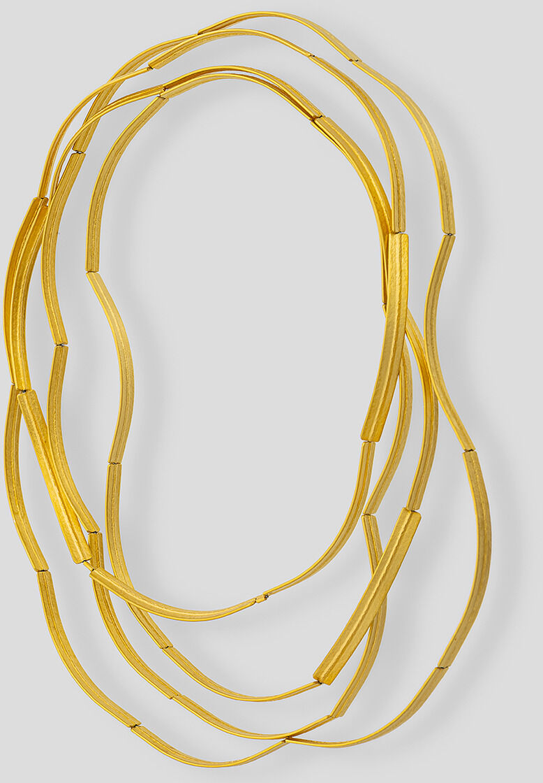 Abgebildet ist die Kette »Bogen«, goldplattiert von Franziska Rappold. Die handgefertigte Halskette besteht aus mehreren feinen, wellenförmigen Elementen aus goldplattiertem Silber und wirkt modern, elegant und filigran. Der Hintergrund ist hellgrau.