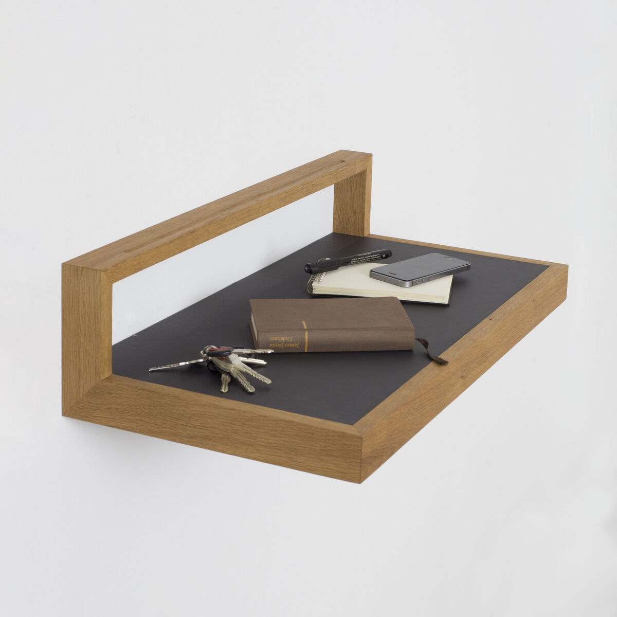 Modernes Ablagebord »buck« in anthrazit mit geöltem Eichenholzrahmen an einer weißen Wand. Auf der Oberfläche liegen Schlüssel, Notizbücher und ein Smartphone. Klare Linien, minimalistisches, funktionales Design, geeignet als Regal, Ablage oder kleines Pult.