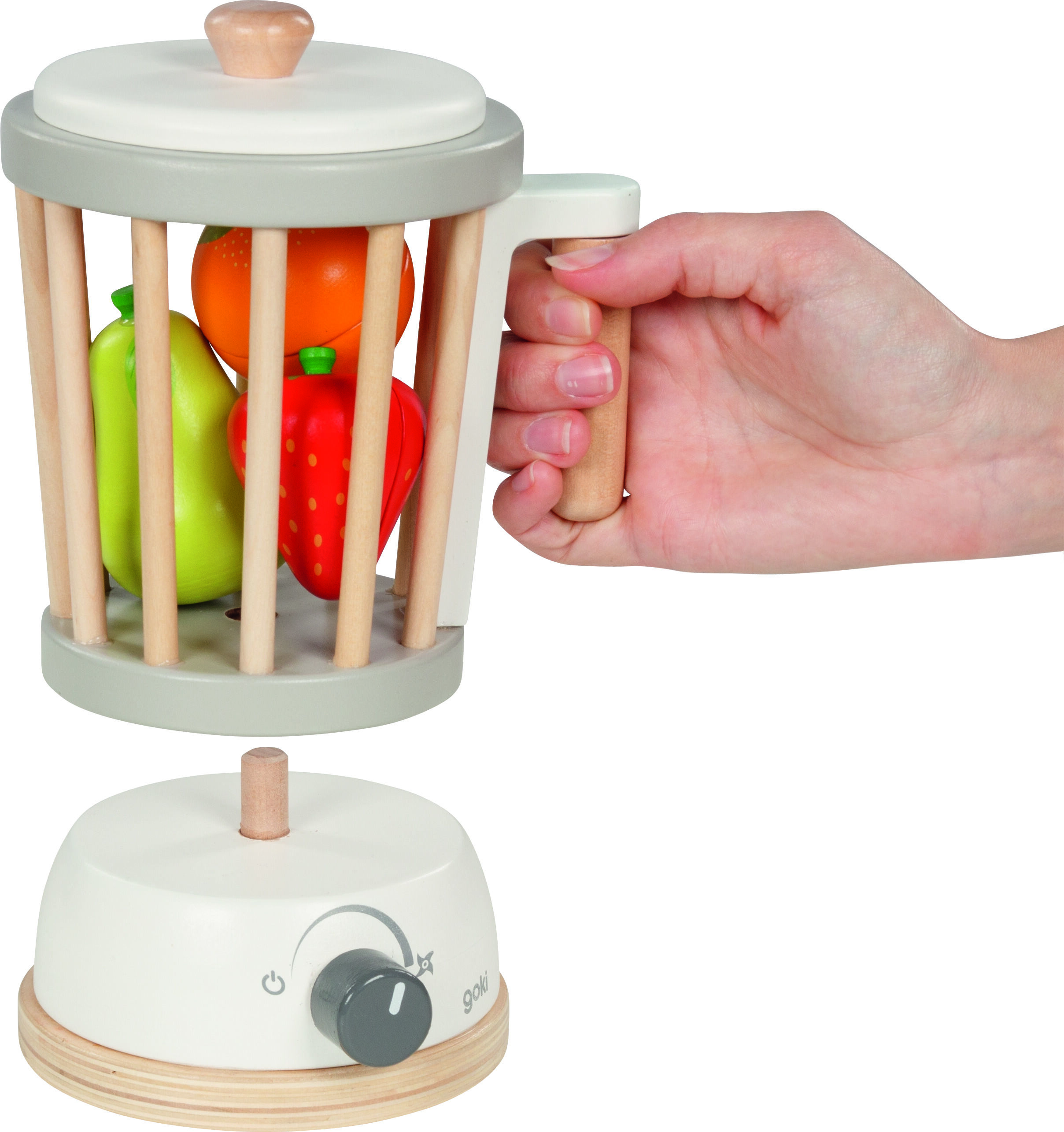 Zu sehen ist ein Holz-Standmixer als Spielzeug. Ein helles, rundes Mixergehäuse mit vertikalen Holzstäben enthält einzeln erkennbare Obstspielzeuge in grün, orange und rot. Eine Kinderhand hält den Griff des Mixers, das Gerät hat einen Drehknopf. Alles besteht aus glatten, unlackierten und farbigen Holzelementen.