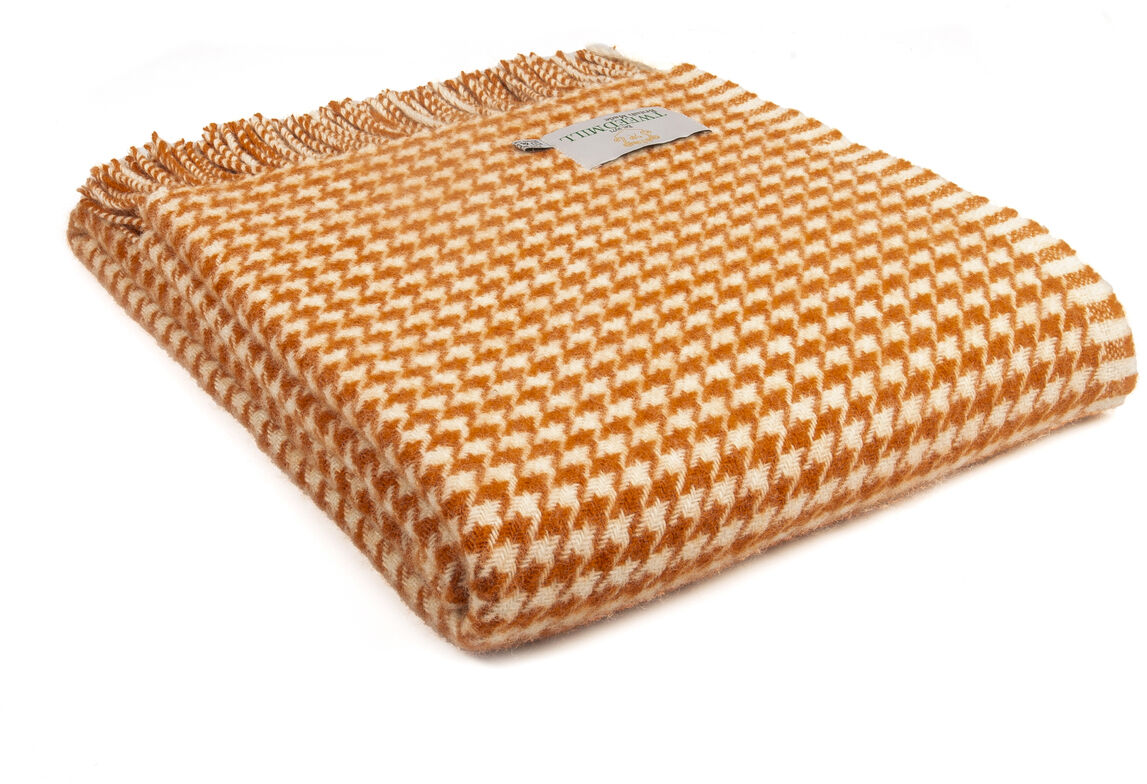 Eine Decke im Hahnentrittmuster in den Farben Orange und Weiß. Die Decke hat Fransen an den Enden und ein Etikett mit der Aufschrift 'Houndstooth'.
