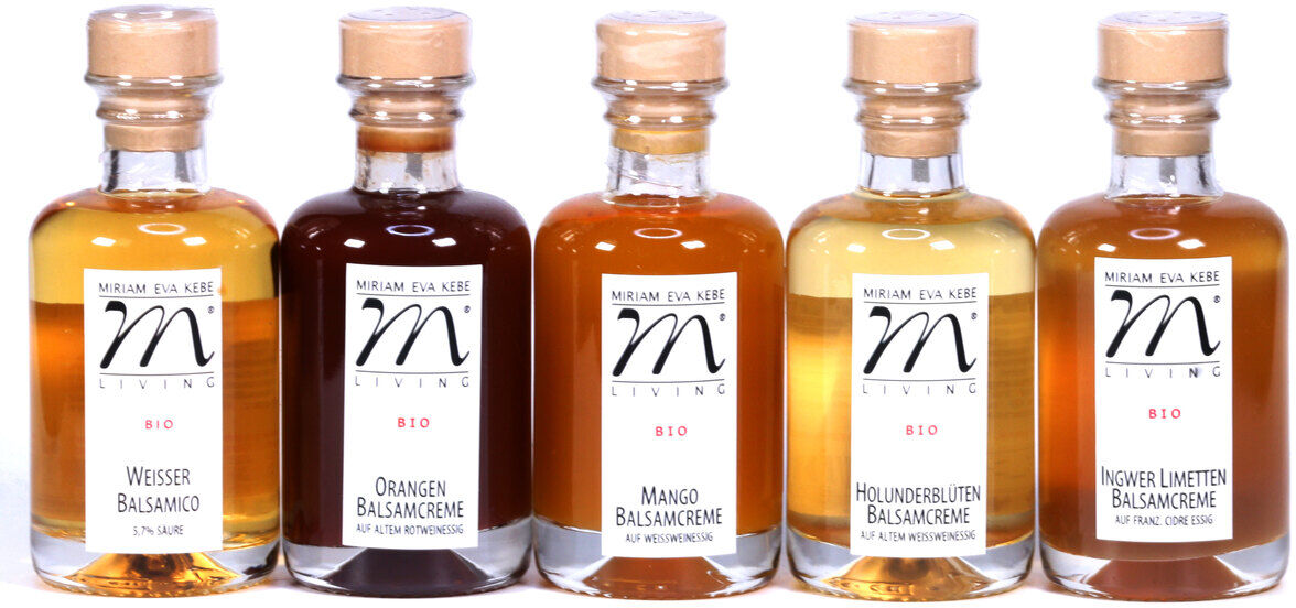 Das Bild zeigt ein Essig-Set »Hell« mit fünf verschiedenen Sorten Balsamico: Weißer Balsamico, Orangen Balsamico, Mango Balsamico, Holunderblüten Balsamico und Ingwer Limetten Balsamico. Jede Flasche hat ein Etikett und einen Holzverschluss.