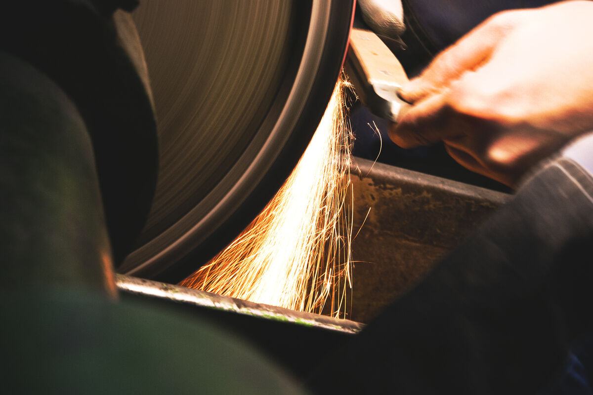 Hände schärfen ein Chinesisches Kochmesser Chai Dao an einem Schleifstein, während Funken sprühen.