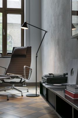 Eine schwarze Stehleuchte der Marke »NJP« steht neben einem braunen Bürostuhl vor einem großen Fenster. Die Lampe hat ein minimalistisches, modernes Design und beleuchtet einen gehobenen Raum mit Schallplattenspieler und dekorativen Accessoires.
