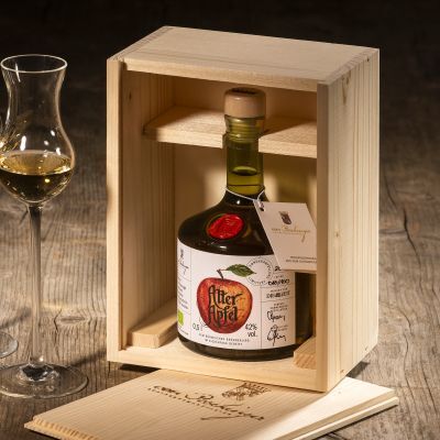Eine Flasche ZEIT-Sonderedition Edelbrand »Alter Apfel« in einer hellen Holzkiste, begleitet von zwei halb gefüllten Schnapsgläsern und einem Notizbuch auf einem rustikalen Holztisch.