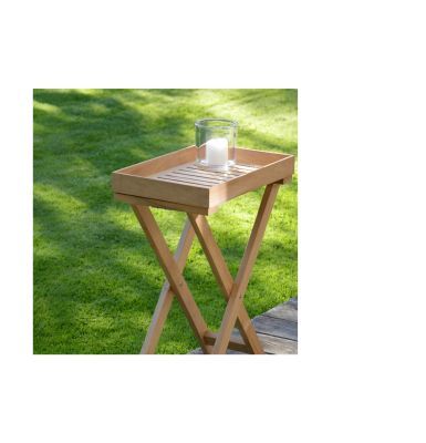 Ein schmaler, klappbarer Beistelltisch aus recyceltem Teakholz steht auf einer Terrasse neben einer Rasenfläche. Auf der abnehmbaren Tablettfläche steht ein Glas mit einer weißen Kerze. Das Holz zeigt natürliche Maserungen und Astlöcher.
