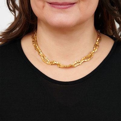 Frau trägt eine goldplattierte Halskette mit würfelförmigen Gliedern über einem schwarzen Oberteil.