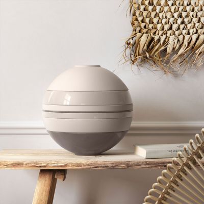 Das Bild zeigt ein modernes Geschirr-Set namens »La Boule«, das aus mehreren runden, ineinander stapelbaren Teilen besteht. Das Set steht auf einem Holztisch vor einer hellen Wand mit einer dekorativen Palme im Hintergrund.